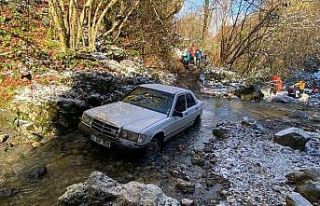 Karlı havada atletli bir adam, dere yatağında otomobilden...